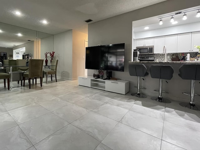 kitchen featuring white cabinets, a breakfast bar, stainless steel microwave, backsplash, and visible vents