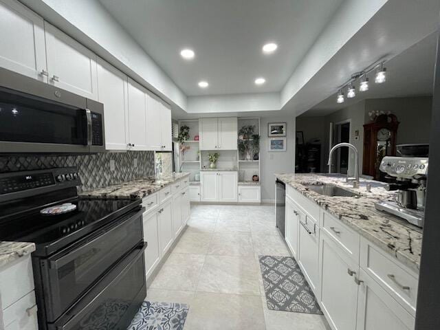 kitchen featuring white cabinets, a sink, stainless steel microwave, light stone countertops, and double oven range