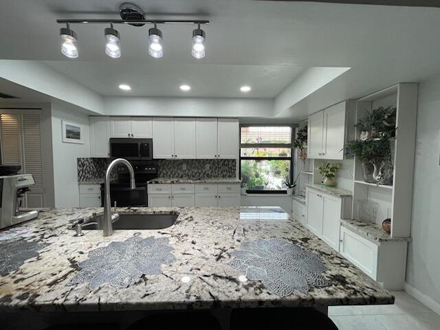 kitchen featuring light stone counters, a sink, a raised ceiling, backsplash, and white cabinetry
