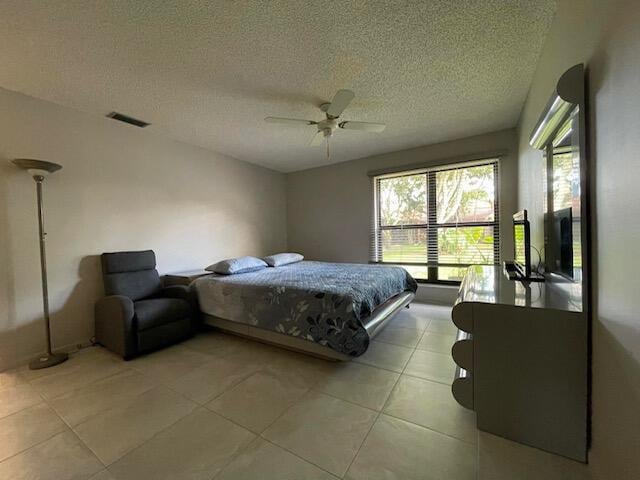 bedroom with a ceiling fan, visible vents, a textured ceiling, and light tile patterned flooring