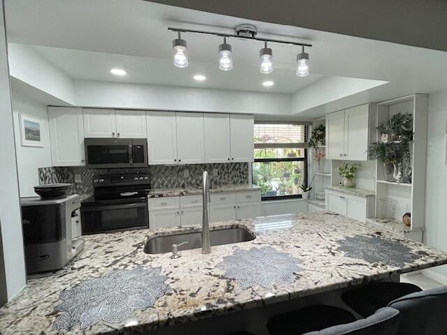 kitchen featuring a breakfast bar, black range with electric stovetop, a sink, stainless steel microwave, and white cabinetry