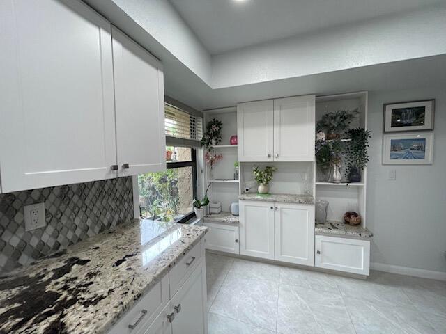 kitchen featuring white cabinets, backsplash, open shelves, and light stone countertops