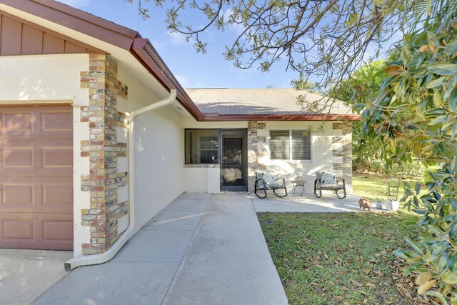 entrance to property featuring a garage, stone siding, and stucco siding