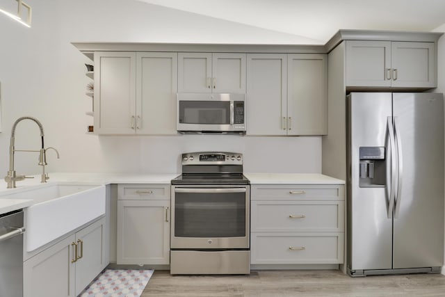 kitchen with a sink, gray cabinetry, vaulted ceiling, stainless steel appliances, and open shelves