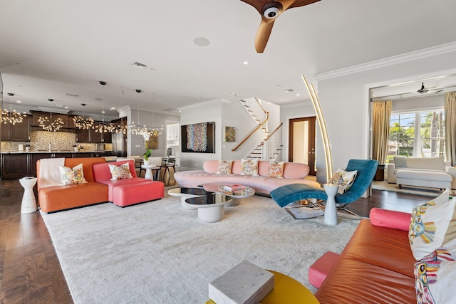 living area featuring visible vents, ornamental molding, ceiling fan with notable chandelier, stairway, and dark wood-style flooring