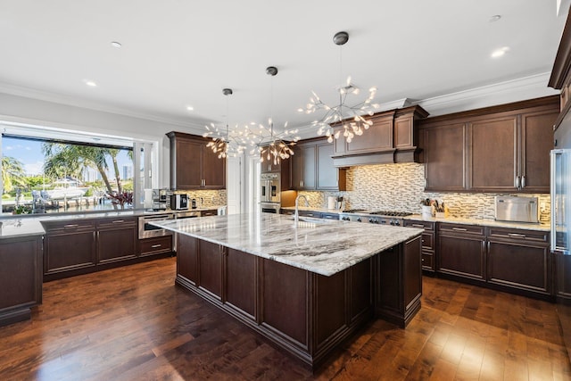 kitchen featuring dark wood-style flooring, crown molding, an inviting chandelier, and a kitchen island with sink