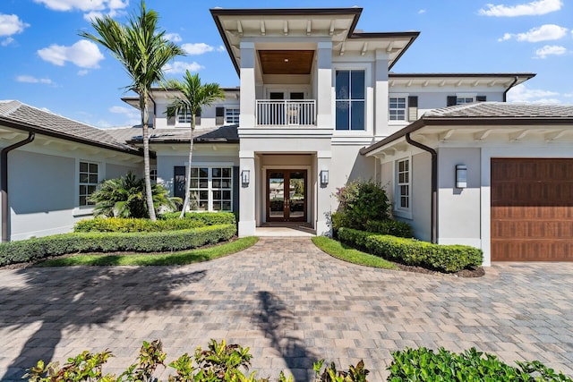 view of front of house featuring a tile roof, stucco siding, french doors, a balcony, and an attached garage