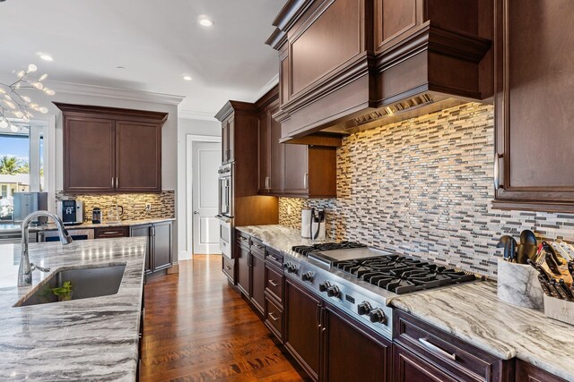 kitchen with light stone countertops, premium range hood, ornamental molding, stainless steel appliances, and a sink