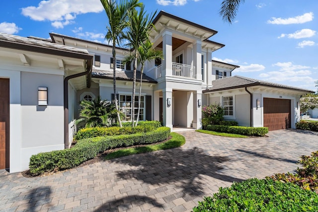 neoclassical home with a balcony, decorative driveway, an attached garage, and stucco siding