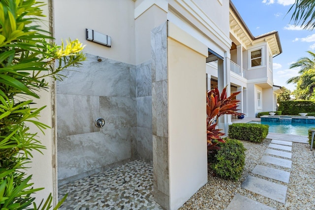 view of side of home featuring stucco siding and a pool with connected hot tub