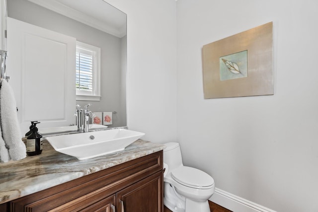 half bathroom featuring baseboards, toilet, vanity, and crown molding