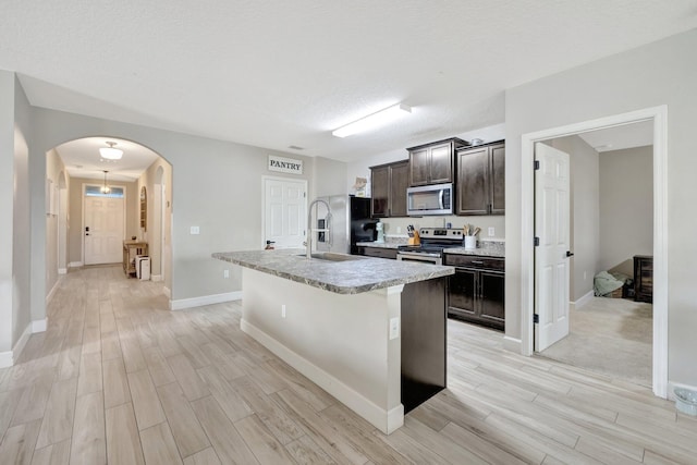 3558 SW Pisano St, Port Saint Lucie, FL 34953 - kitchen with wood finish floors, a kitchen island with sink, arched walkways, dark brown cabinetry, and appliances with stainless steel finishes