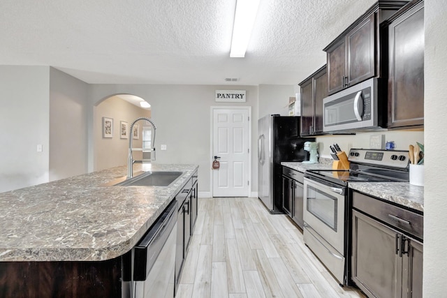 3558 SW Pisano St, Port Saint Lucie, FL 34953 - kitchen with a center island with sink, arched walkways, a sink, dark brown cabinetry, and appliances with stainless steel finishes