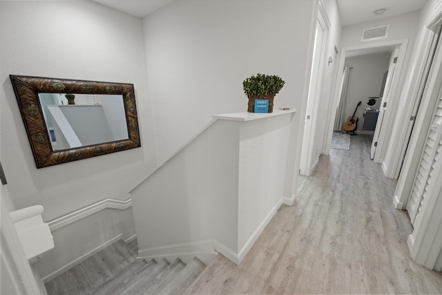 corridor with an upstairs landing, visible vents, light wood-type flooring, and baseboards