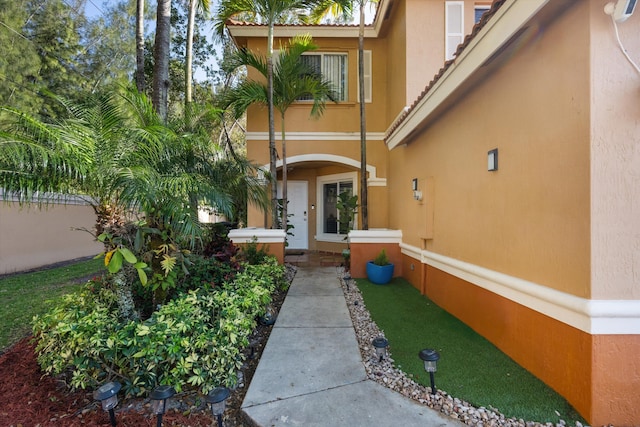 view of exterior entry with a tile roof, fence, and stucco siding