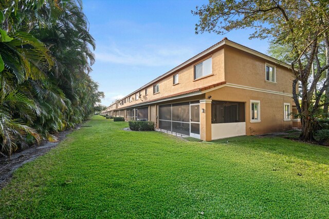 rear view of property featuring stucco siding, a yard, and a sunroom