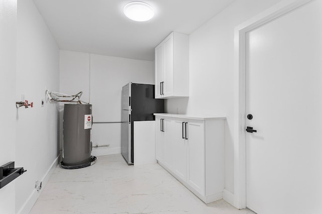 6887 Osborne Dr, Lake Worth, FL 33462 - kitchen featuring electric water heater, freestanding refrigerator, white cabinetry, light marble finish flooring, and baseboards