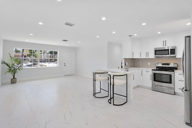 6887 Osborne Dr, Lake Worth, FL 33462 - kitchen featuring stainless steel appliances, light marble finish floors, a peninsula, white cabinets, and recessed lighting