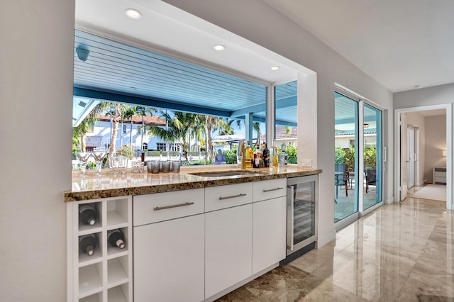 bar with marble finish floor, recessed lighting, bar area, a sink, and beverage cooler