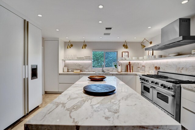 kitchen featuring white cabinets, range with two ovens, a center island, and wall chimney exhaust hood