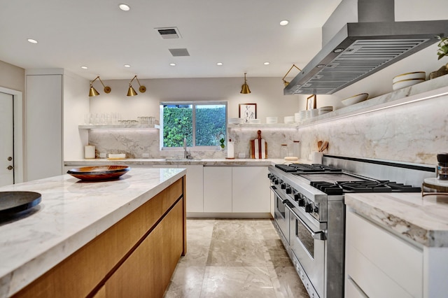 kitchen with light stone counters, a sink, double oven range, wall chimney range hood, and visible vents