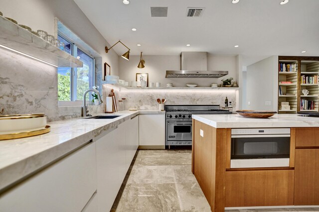 kitchen featuring a sink, wall chimney range hood, visible vents, white cabinets, and designer stove