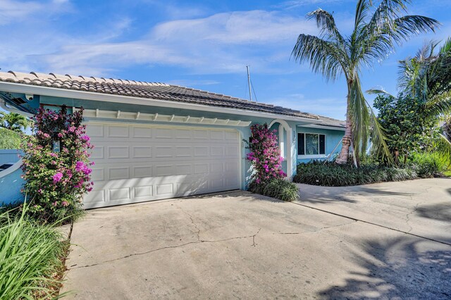 single story home featuring a tile roof, concrete driveway, stucco siding, and an attached garage