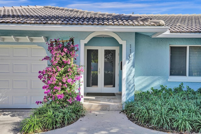 property entrance with a tile roof, stucco siding, a garage, and french doors