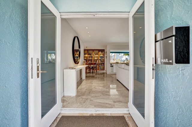 hall featuring marble finish floor, a textured wall, and french doors