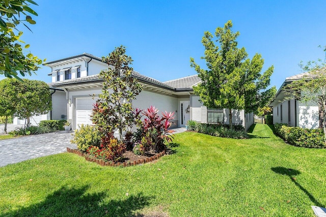 view of front facade featuring a front yard, decorative driveway, a garage, and stucco siding