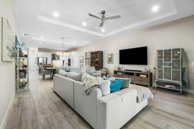 living room featuring baseboards, wood tiled floor, recessed lighting, a raised ceiling, and ceiling fan with notable chandelier