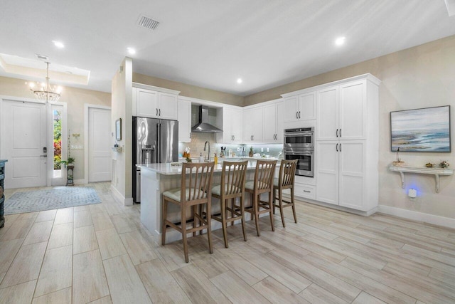 kitchen with visible vents, wall chimney range hood, white cabinetry, stainless steel appliances, and light countertops