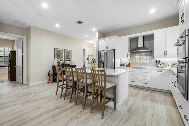kitchen with a center island with sink, wall chimney range hood, high quality fridge, light countertops, and decorative backsplash