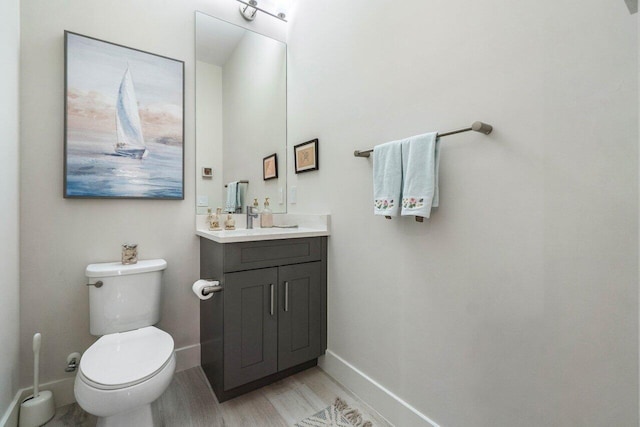 bathroom with toilet, vanity, baseboards, and wood finished floors