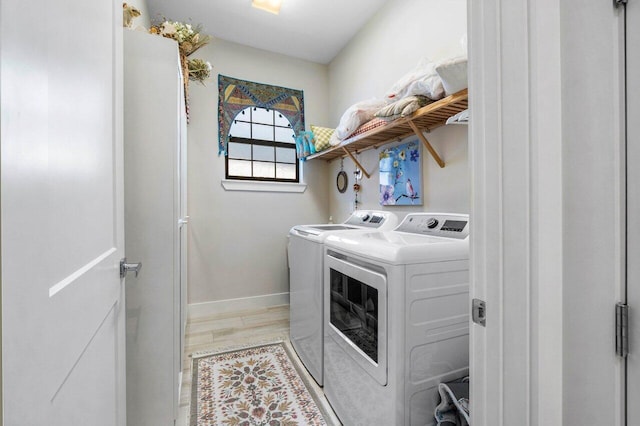clothes washing area featuring baseboards, light wood-style flooring, laundry area, and washing machine and clothes dryer