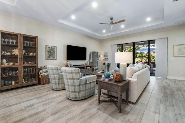 living room with visible vents, ceiling fan, light wood-type flooring, and a tray ceiling
