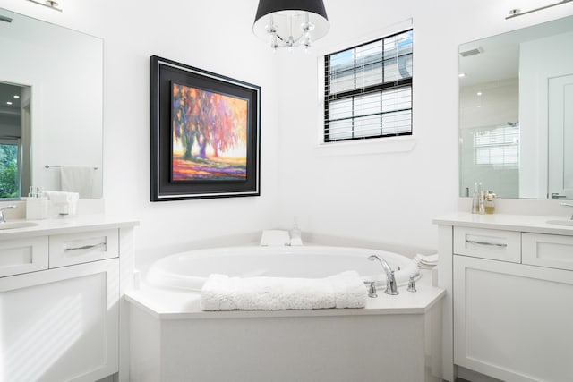 full bath featuring a shower stall, two vanities, a garden tub, and a sink