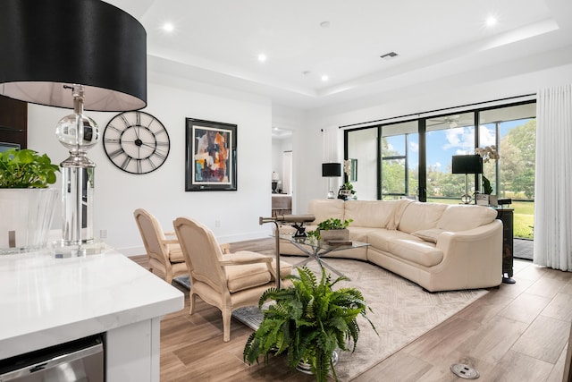 living room featuring visible vents, baseboards, recessed lighting, light wood-style flooring, and a raised ceiling