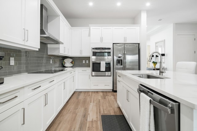 kitchen with a sink, stainless steel appliances, tasteful backsplash, and wall chimney range hood