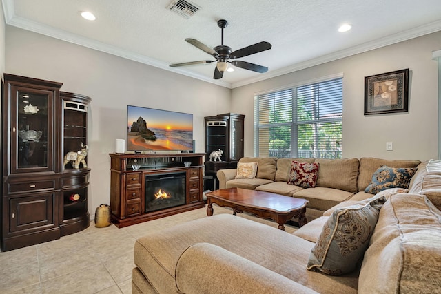living room with light tile patterned floors, visible vents, ceiling fan, a glass covered fireplace, and crown molding