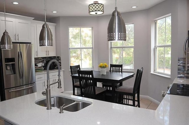 kitchen with plenty of natural light, a sink, light countertops, stainless steel refrigerator with ice dispenser, and backsplash
