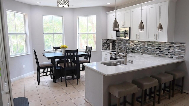 kitchen featuring stainless steel appliances, light countertops, white cabinetry, a kitchen breakfast bar, and backsplash