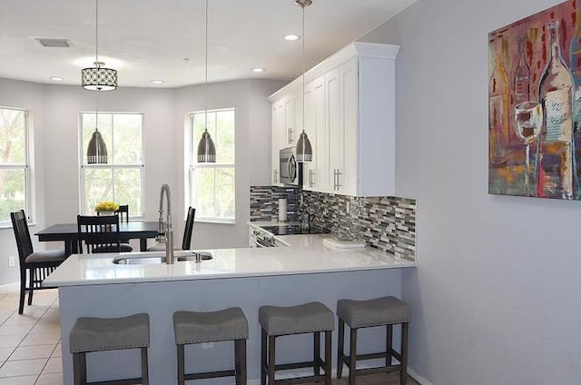 kitchen featuring a peninsula, a sink, stove, stainless steel microwave, and tasteful backsplash