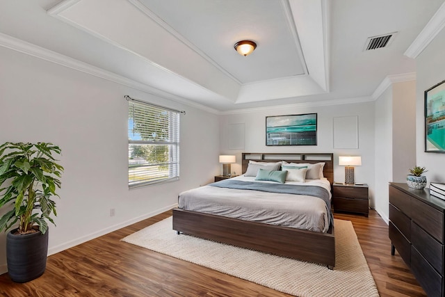 bedroom featuring visible vents, baseboards, crown molding, a tray ceiling, and wood finished floors