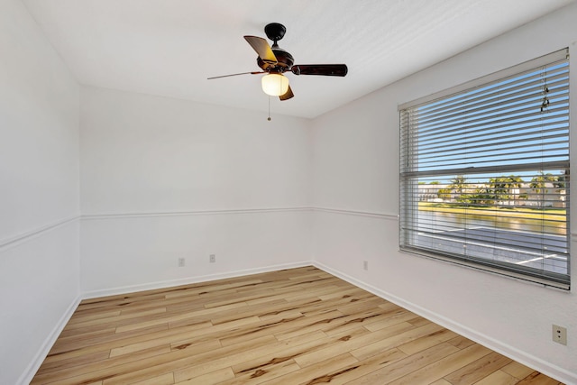 spare room with a water view, baseboards, light wood finished floors, and a ceiling fan