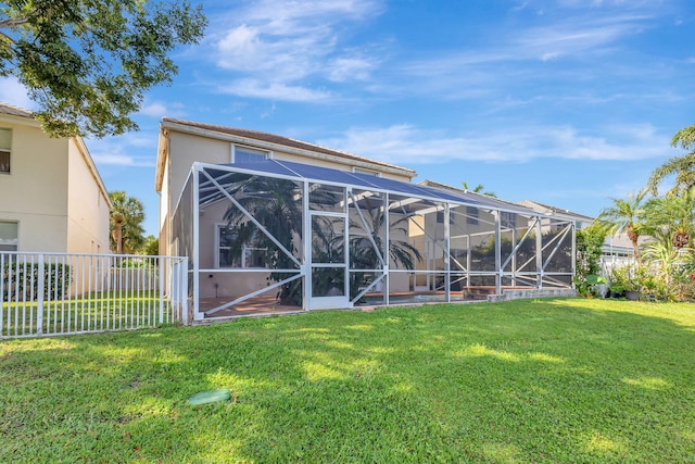 back of property featuring fence, stucco siding, a lawn, and glass enclosure