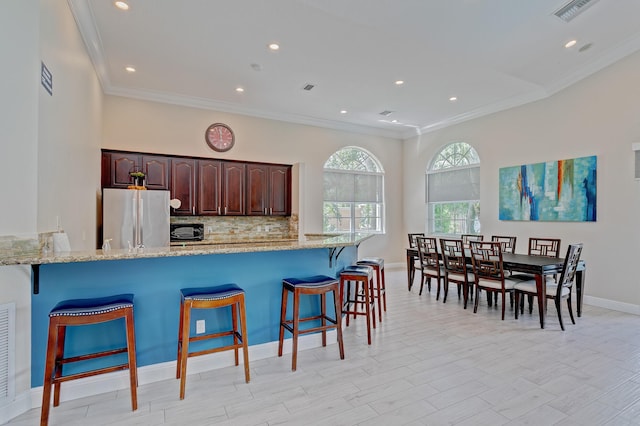 kitchen with light stone counters, freestanding refrigerator, visible vents, and a kitchen breakfast bar
