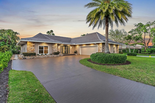 single story home featuring stone siding, a garage, driveway, and a front yard