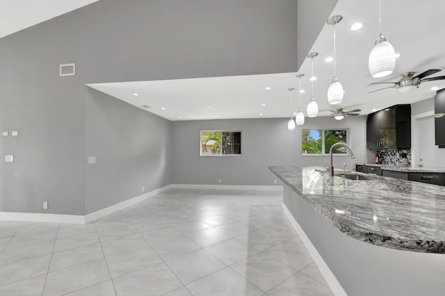 kitchen with visible vents, a ceiling fan, a sink, dark cabinets, and light stone counters