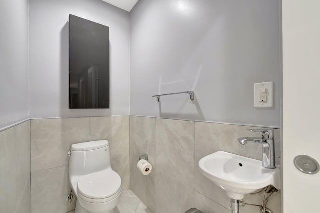 bathroom with tile walls, a sink, toilet, and wainscoting
